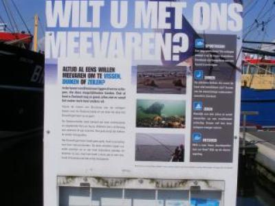 Bord op de kade van de vissershaven met de titel 'Wilt u met ons meevaren' en daaronder informatieve tekst en foto's.