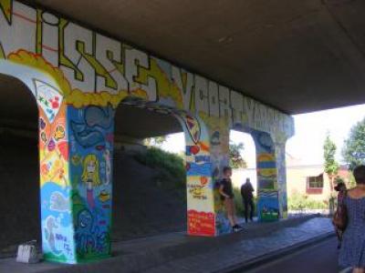 viaduct met kleurige beschildering en jongeren die tegen de pilaren staan.