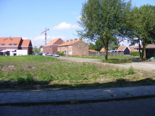 braakliggend terrein begroeid met onkruid aan de Koningin Julianastraat met op achtergrond bebouwing